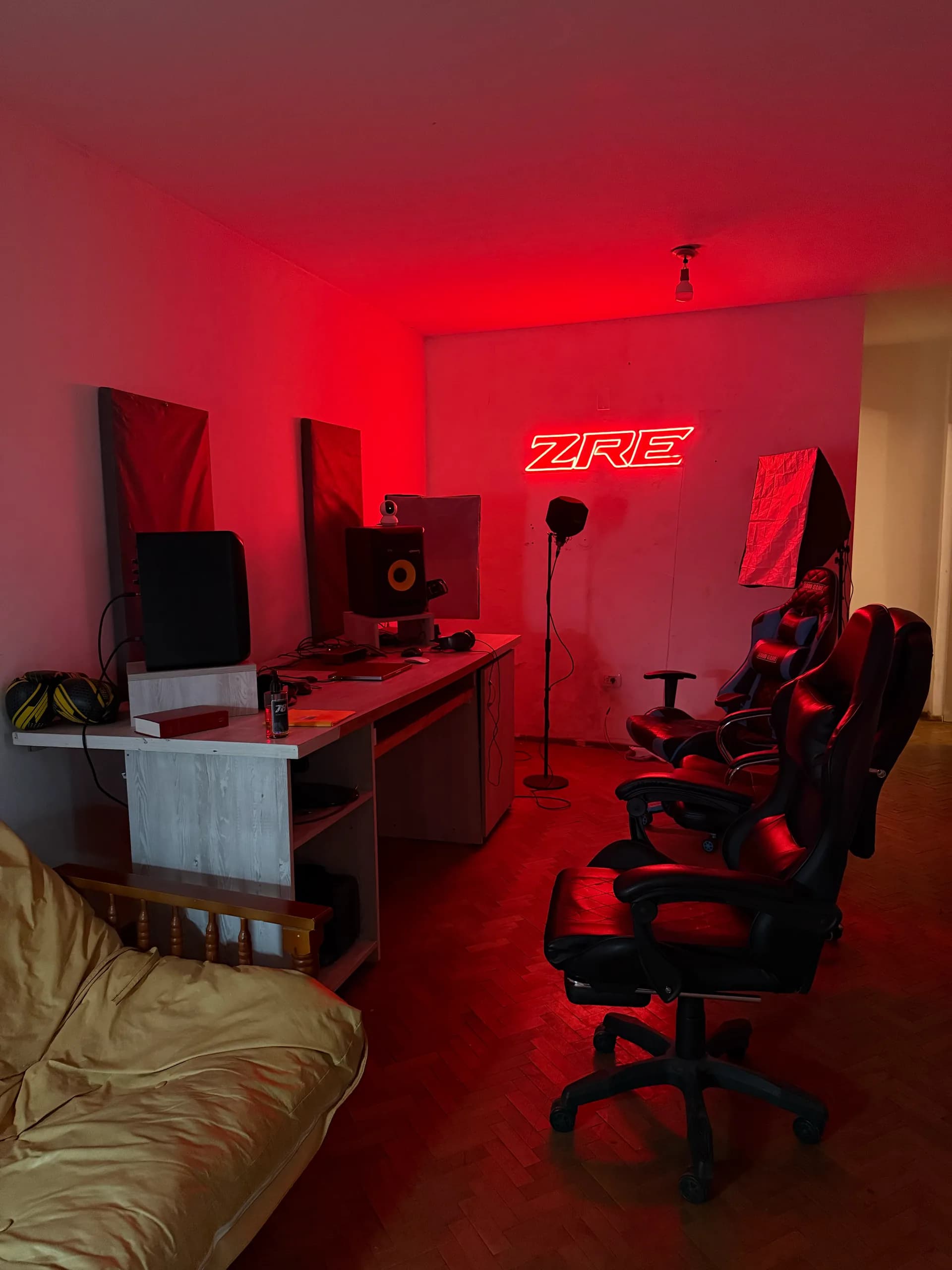 El estudio de Zonarojaestudio iluminado en rojo, con un cartel de neón ZRE en la pared, escritorio con monitores de audio, micrófono de pie, softbox y dos butacas